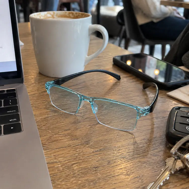 Blue clear frame glasses on a cafe table beside laptop, phone, and coffee